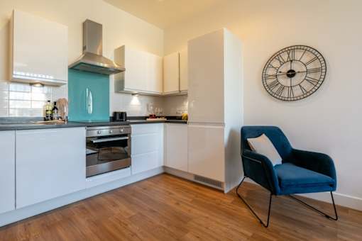 a kitchen with a chair and a clock on the wall at The Keel Apartments, Liverpool