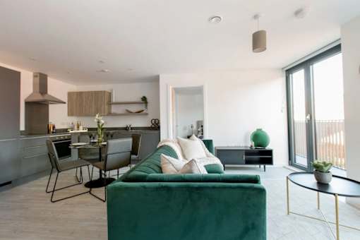 a living room with a green couch and a kitchen with a table and chairs at Vox Apartments, Manchester