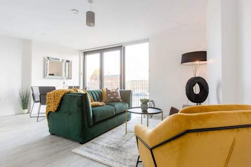 a living room with a green couch and a large window at Vox Apartments, Manchester