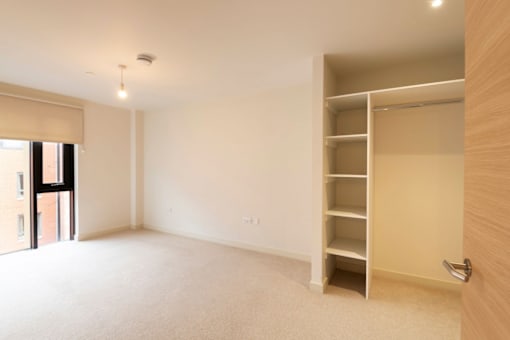 an empty living room with a book shelf in the corner at The Trilogy Apartments, Manchester