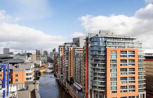 A river flows through a city with modern buildings on either side.at Slate Yard Apartments, Salford, M3 5EX