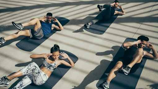 Three people are exercising on black mats in a sunlit room.