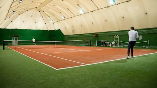 A man is playing tennis on a court with a green wall in the background.