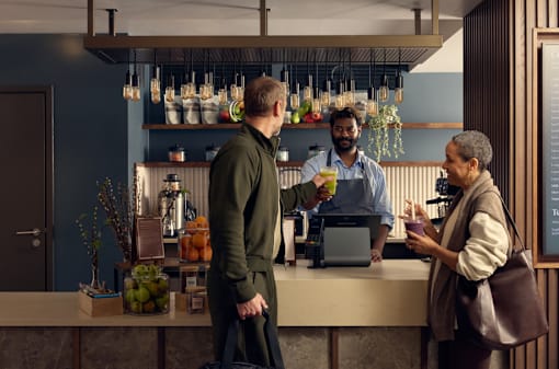 A man in a green sweater is standing at a bar with a bartender.