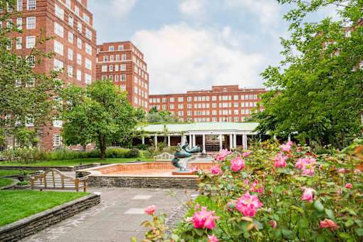 A garden with a fountain and roses in front of a red brick building.