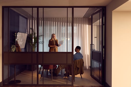 Two people are having a conversation in a room with a glass wall.
