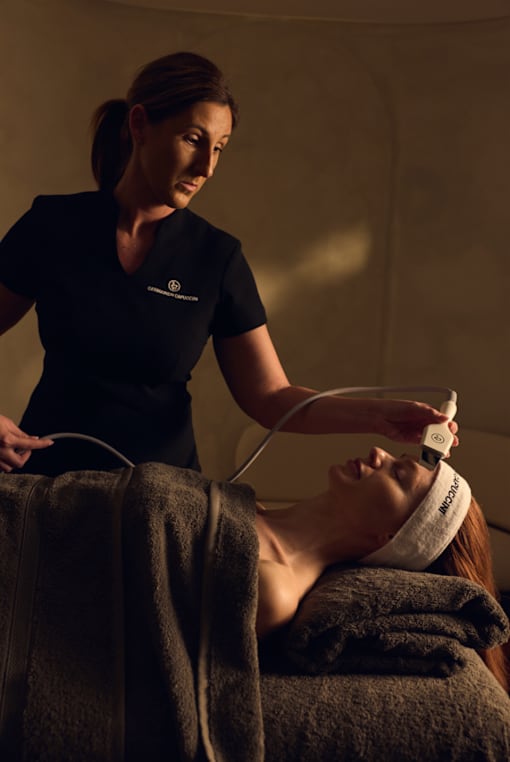 A woman in a black shirt is using a device on another woman's forehead.