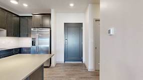 A dark grey front door next to a modern kitchen with dark wooden cabinets.