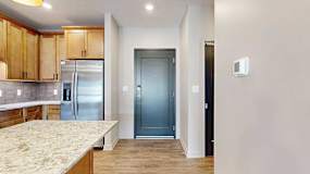 a dark grey front door next to a modern kitchen with wooden cabinets and stainless steel appliances