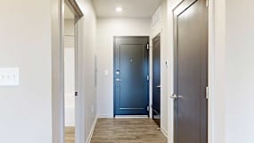 Front door view with wooden vinyl flooring, flanked by doorways to bathroom and coat closet.