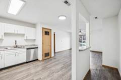 A kitchen with white cabinets open to a spacious living room with hardwood-style flooring.