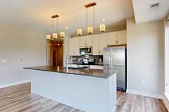 A kitchen with white wooden cabinets, quartz countertops, a large island, stainless steel appliances, and a designer backsplash.