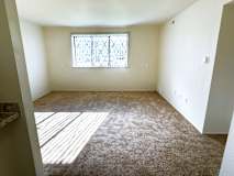 A living room with a carpeted floor and a window with bars.