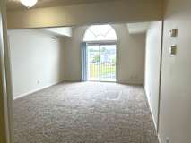 A spacious living room with a carpeted floor and a large arched window.