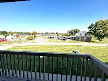 A view from a balcony overlooking a grassy area with a building in the distance.