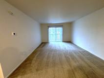 A living room with a carpeted floor and a window with blinds.