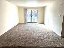 A living room with a carpeted floor and a sliding glass door leading to a balcony.