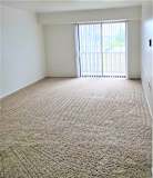 A living room with a carpeted floor and a sliding glass door.