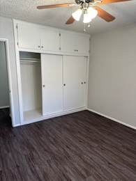 A room with a ceiling fan and built-in cabinets.