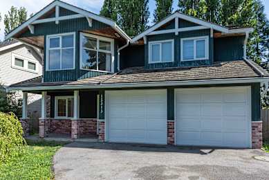 A two-story house with a green roof and white garage doors.
