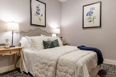 A bedroom with a bed, two lamps, and two framed pictures on the wall.