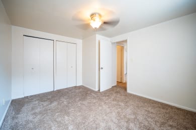 a bedroom with white walls and carpet and a ceiling fan