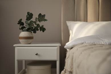 A white table with a plant on it sits next to a bed.
