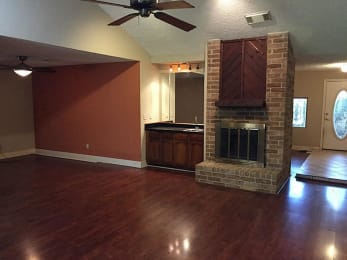 an empty living room with a brick fireplace and wooden floors