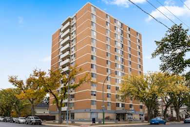A tall apartment building with a parking lot in front.