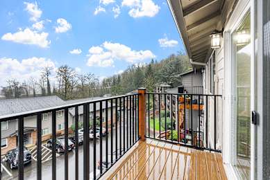 A balcony with a black railing and a view of a parking lot and trees.