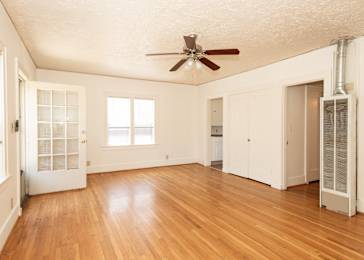 A room with a ceiling fan and wood flooring.