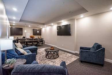 Living area with sofa, accent chairs, coffee table, wall mounted television and carpet flooring at Heartland Flats Alliance.