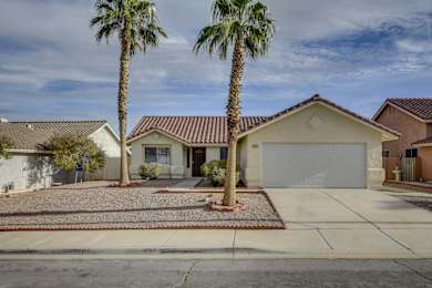 A house with a red tile roof and a white garage door is surrounded by palm trees.
