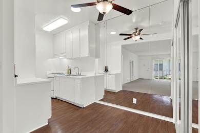 A white kitchen with a wooden floor and a ceiling fan. at Olive Tree Apartments, Torrance, CA