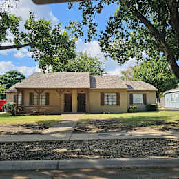 A yellow house with a brown roof and a tree in front.