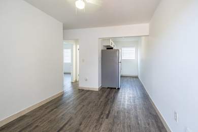A room with a grey fridge and wooden floors.