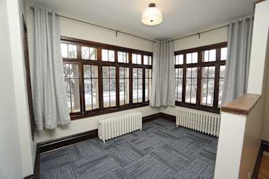 A room with a grey carpet and a window with curtains.