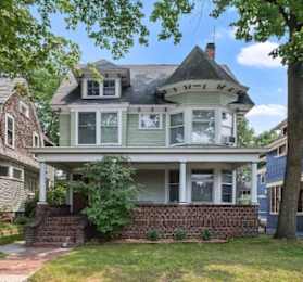 A Victorian style house with a grey front and a brick wall.