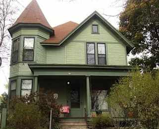 A green house with a red roof and a porch.