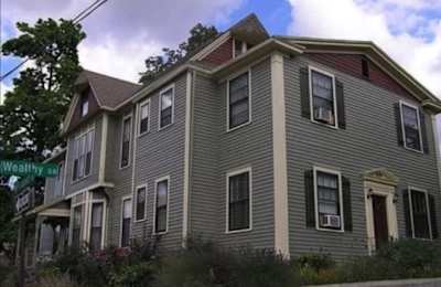 A grey house with a red roof and a sign that says Wealthy St.