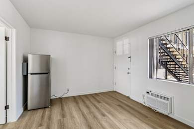 A room with a stainless steel refrigerator and a wooden floor.