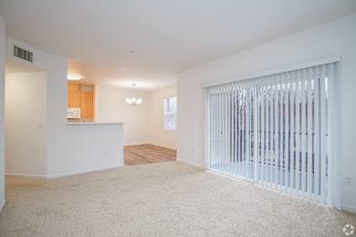 A spacious living room with a white carpet and a sliding glass door.