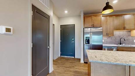A front entryway next to a modern kitchen with warm wooden cabinets and stainless steel appliances.