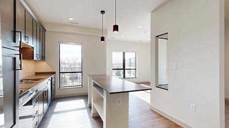 A kitchen with dark wooden cabinets, quartz countertops, a tile backsplash, an island, and a window over the kitchen sink.