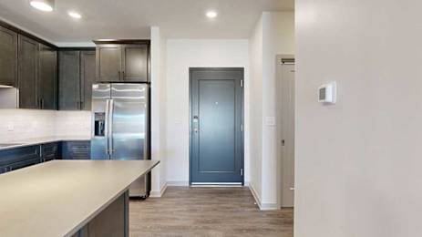 A dark grey front door next to a modern kitchen with dark wooden cabinets.