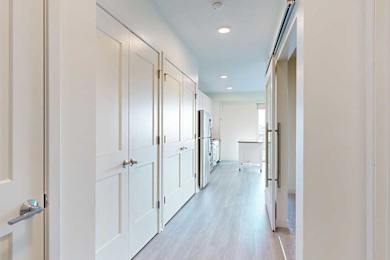 Bright, modern kitchen with sleek light wood flooring, white cabinets on the left, and stainless steel appliances.