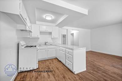 A white kitchen with wooden floors and a logo for Beachfront Property Management in the bottom left corner.