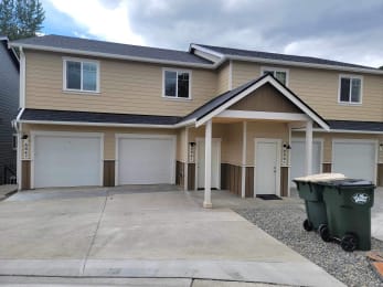 a beige house with white garage doors and a gravel driveway