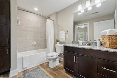 A white toilet sits in a bathroom with a white tub and a white shower curtain.