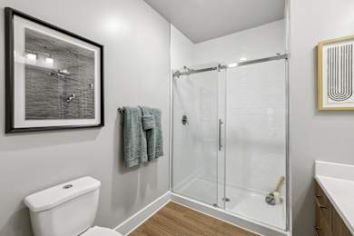 A bathroom with a toilet, a shower with a glass door, and a picture on the wall.